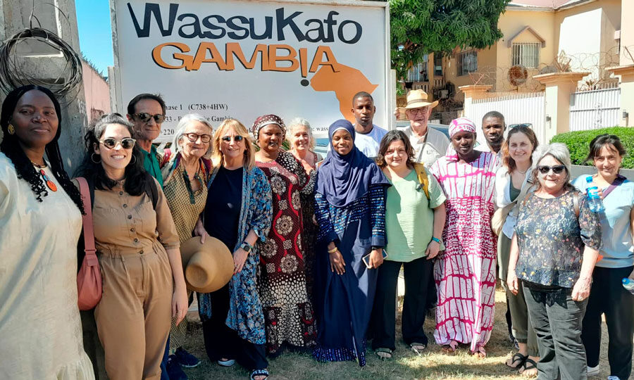 Foto de grup de la delegació que ha viatjat a Gàmbia amb representants de Wassu Gambia Kafo, davant del cartell de l'entitat